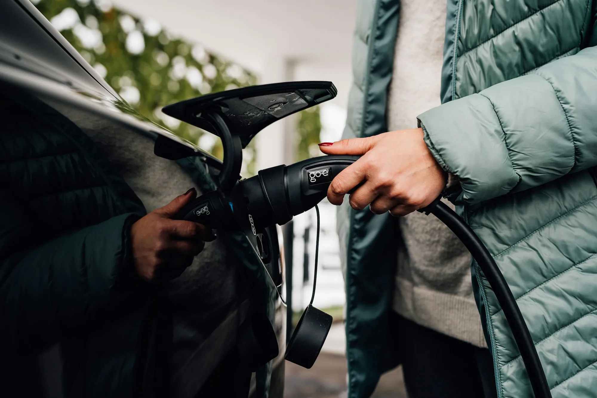 Hand holding an EV charging plug beside a parked car